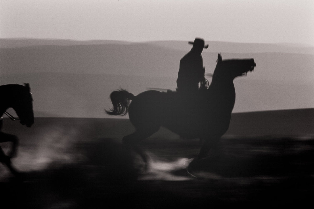 A cowboy riding fast across the open plain on a horse in the american west