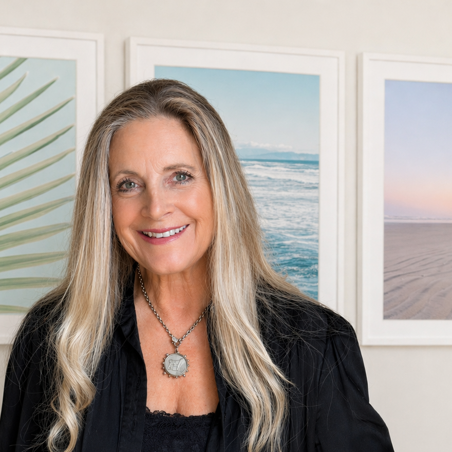 Jules Frazier in a black outfit standing in front of beach-themed wall art from her Coastal Collection