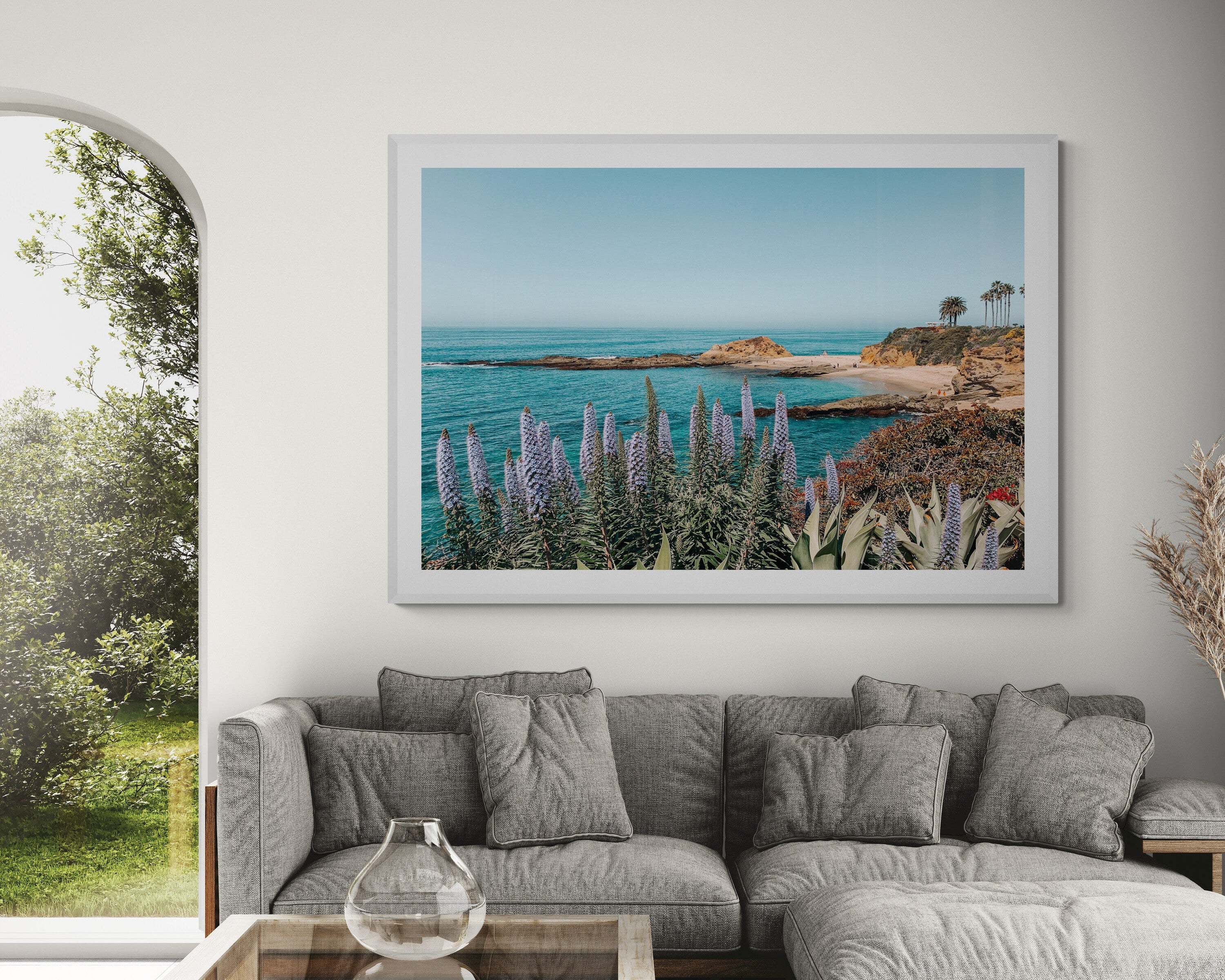 Gray sectional sofa in a living room with a large framed picture of a coastal scene on the wall.