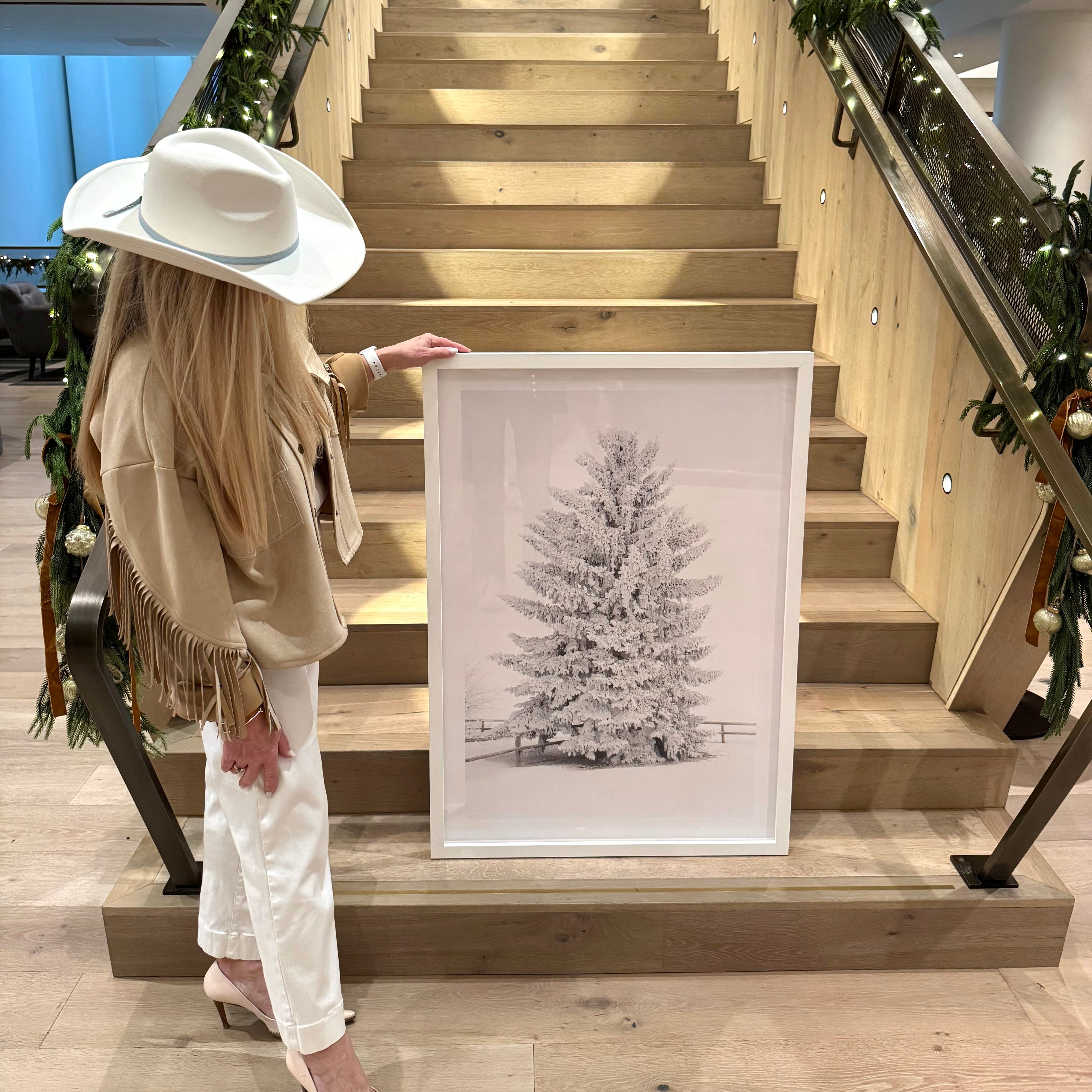 Jules Frazier holding a framed picture of a Christmas tree on a staircase decorated with greenery.