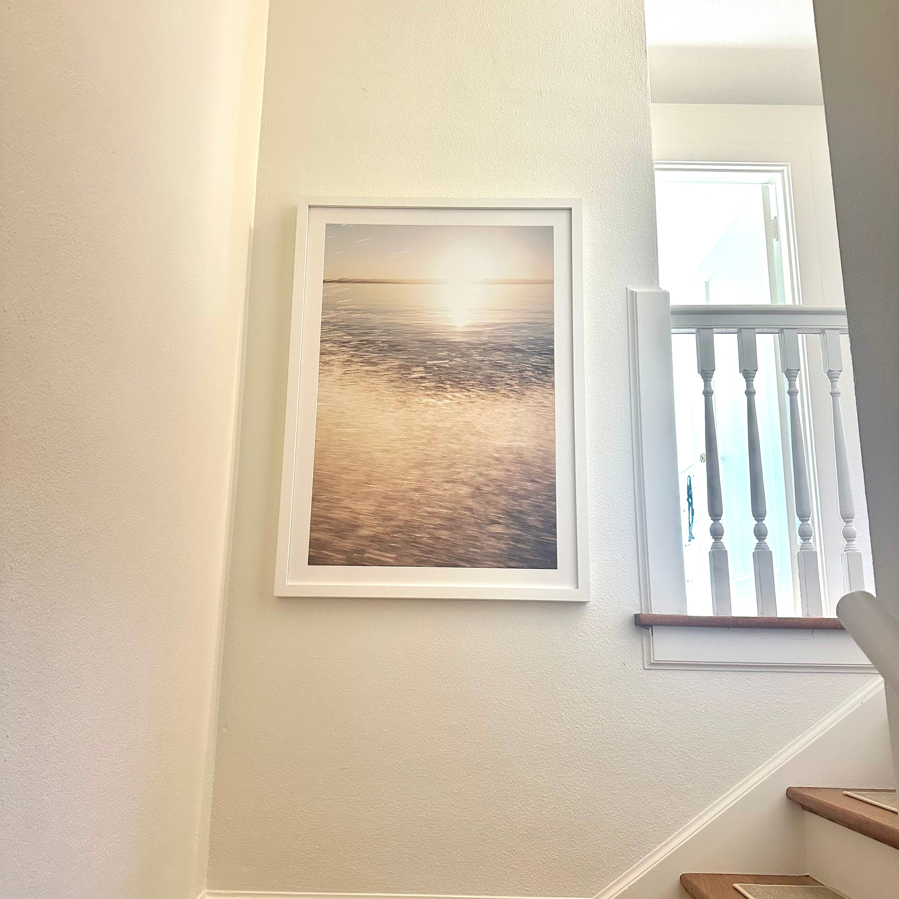Framed artwork on a wall next to a staircase with a window in the background