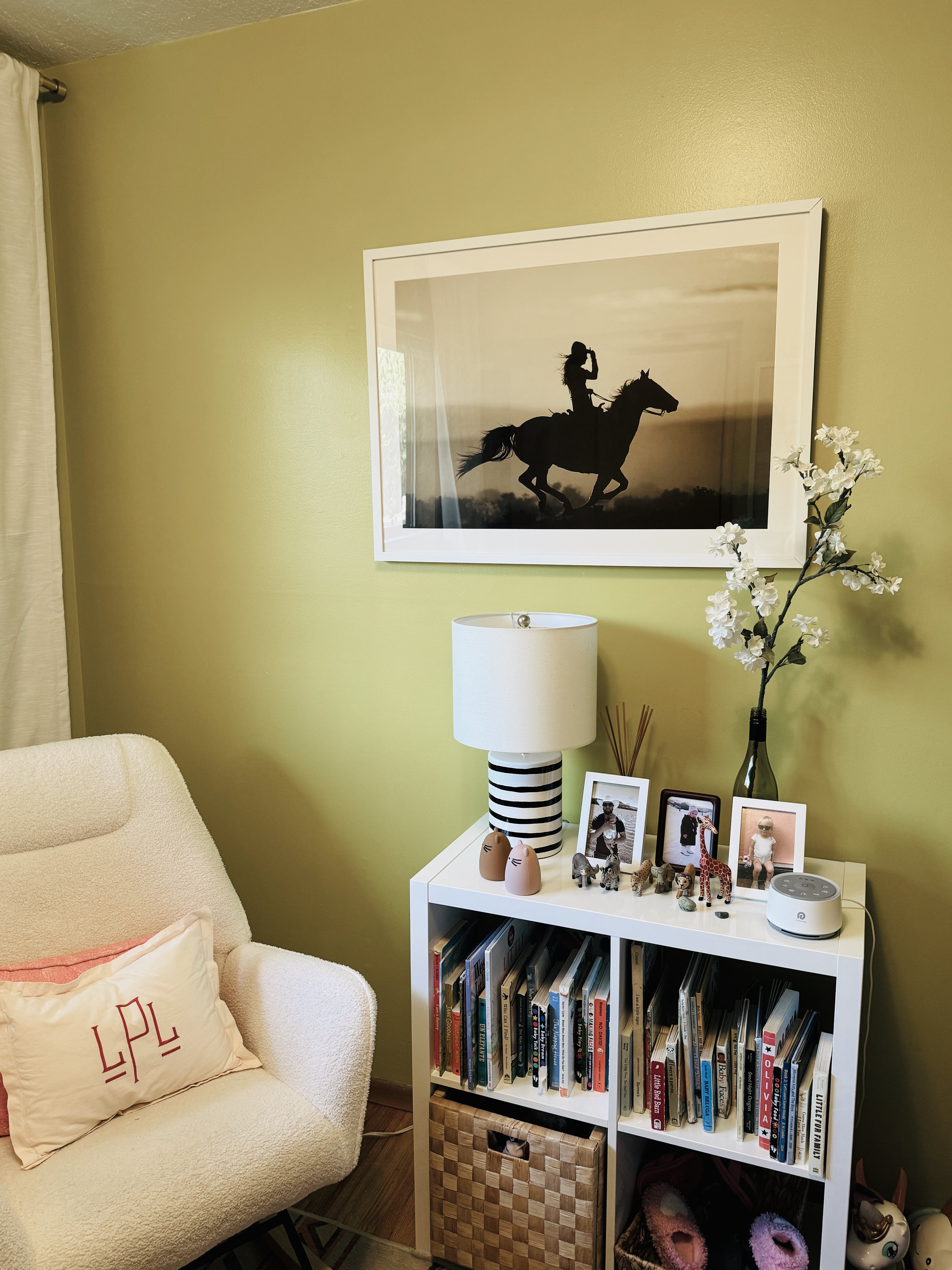 Living room with a white armchair, bookshelf, and framed picture of a horse and rider on a green wall.