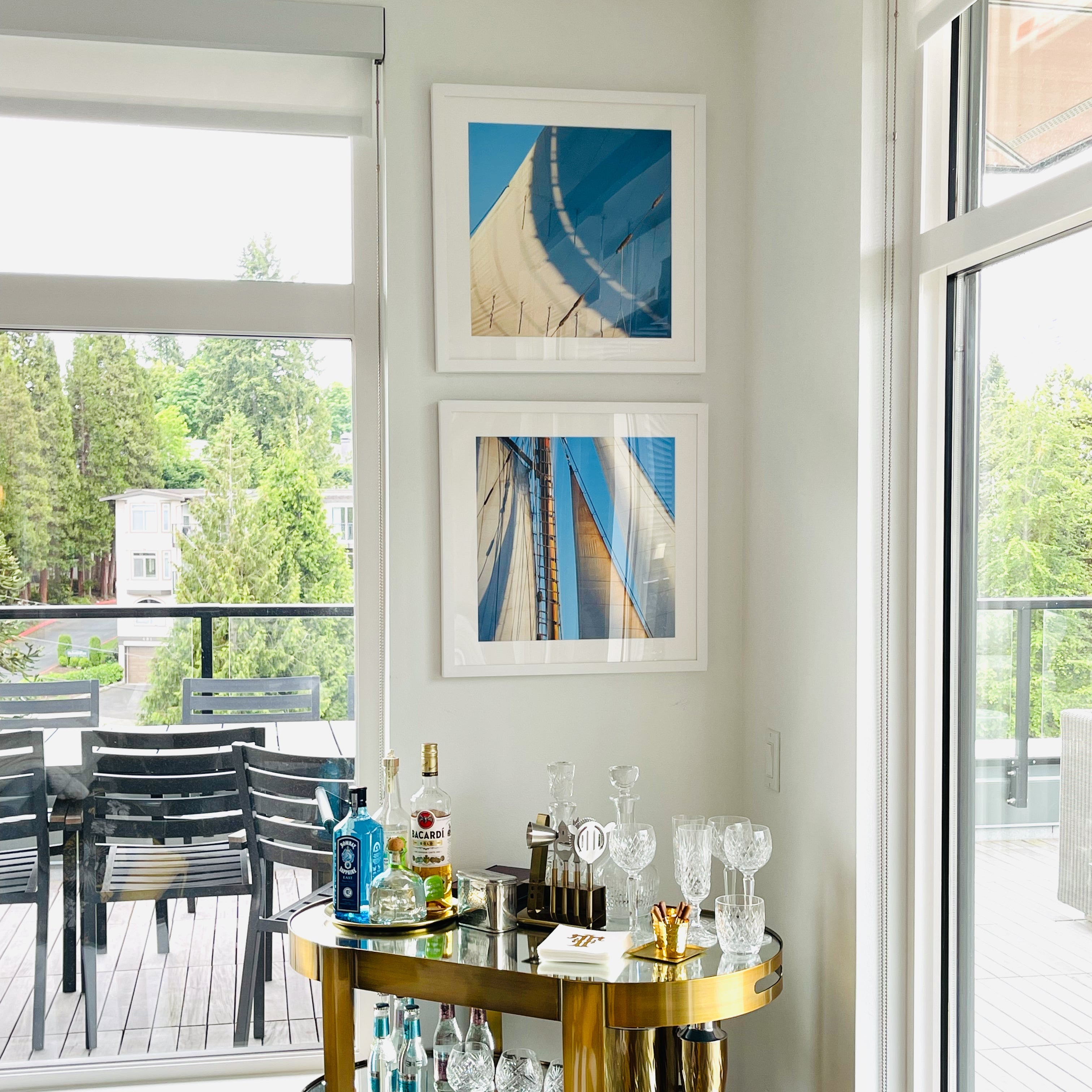 Modern home bar setup with a gold bar cart, bottles, and glasses in a room with large windows.