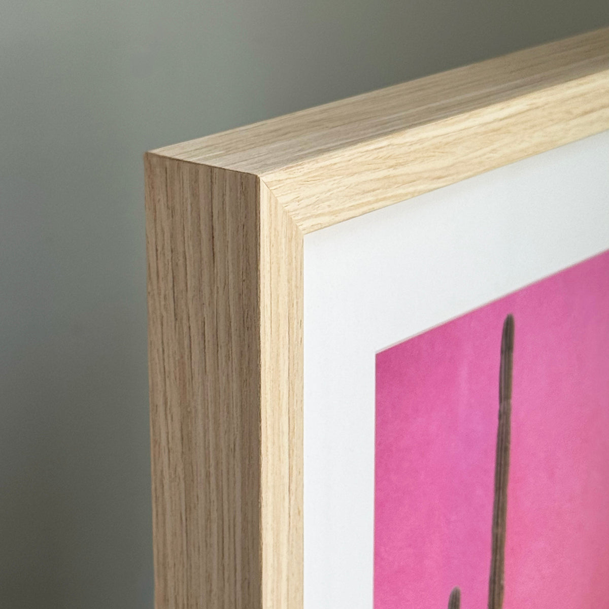 Close-up of a wooden picture frame with a pink artwork inside on a gray background