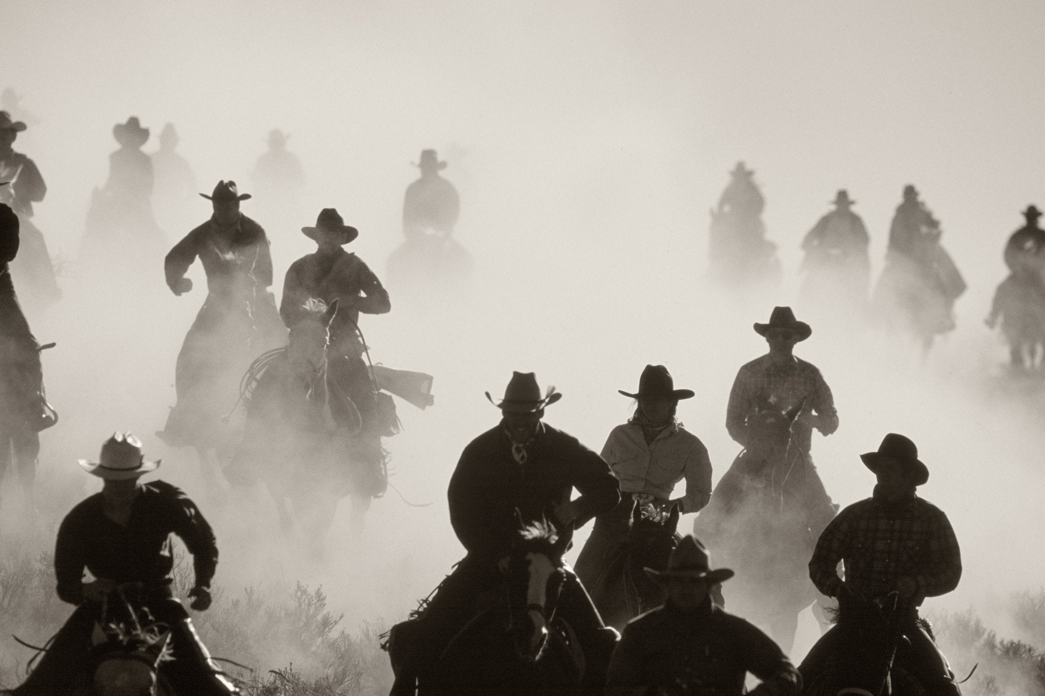 Silhouette of cowboys on horseback charging through a cloud of dust by Jules Frazier
