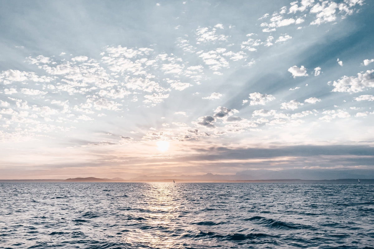 Sunrise or sunset over a calm sea with scattered clouds