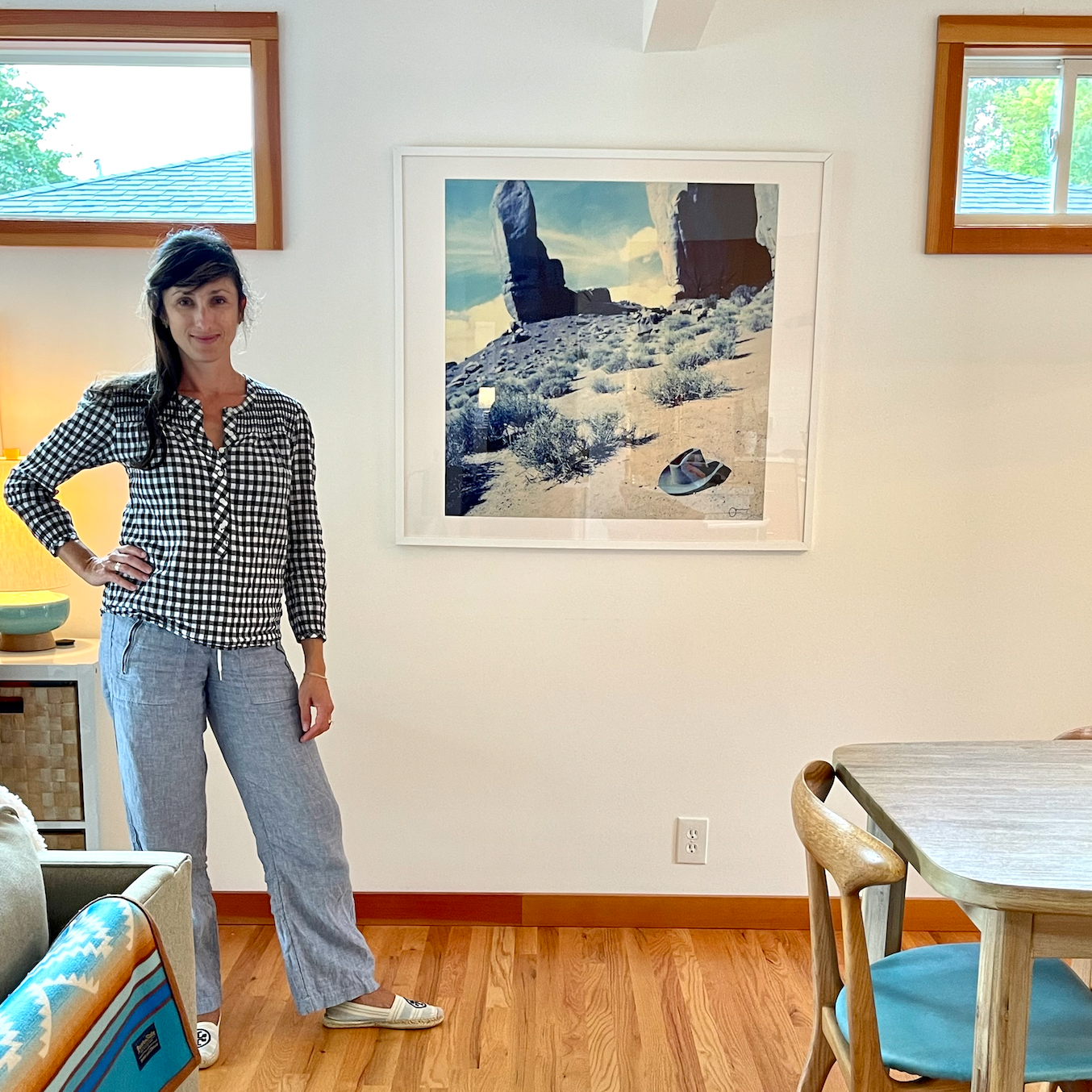 Woman standing in a room with a painting of a desert landscape on the wall.