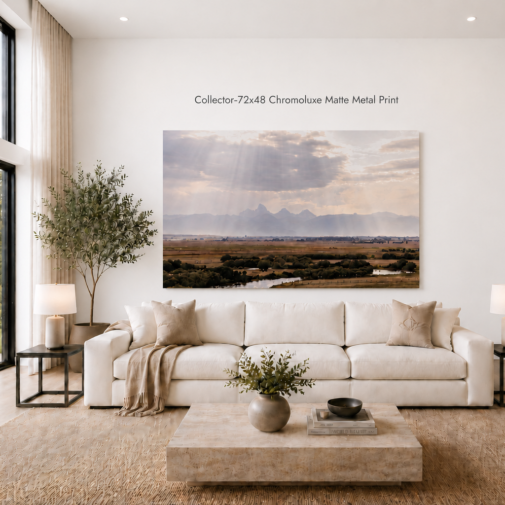 A large landscape art print hangs on a white wall above a white sofa in a modern living room. The print depicts a scenic valley with mountains, clouds, and sun rays, with text above reading 'Collector-72x48 Chromoline Matte Metal Print'.