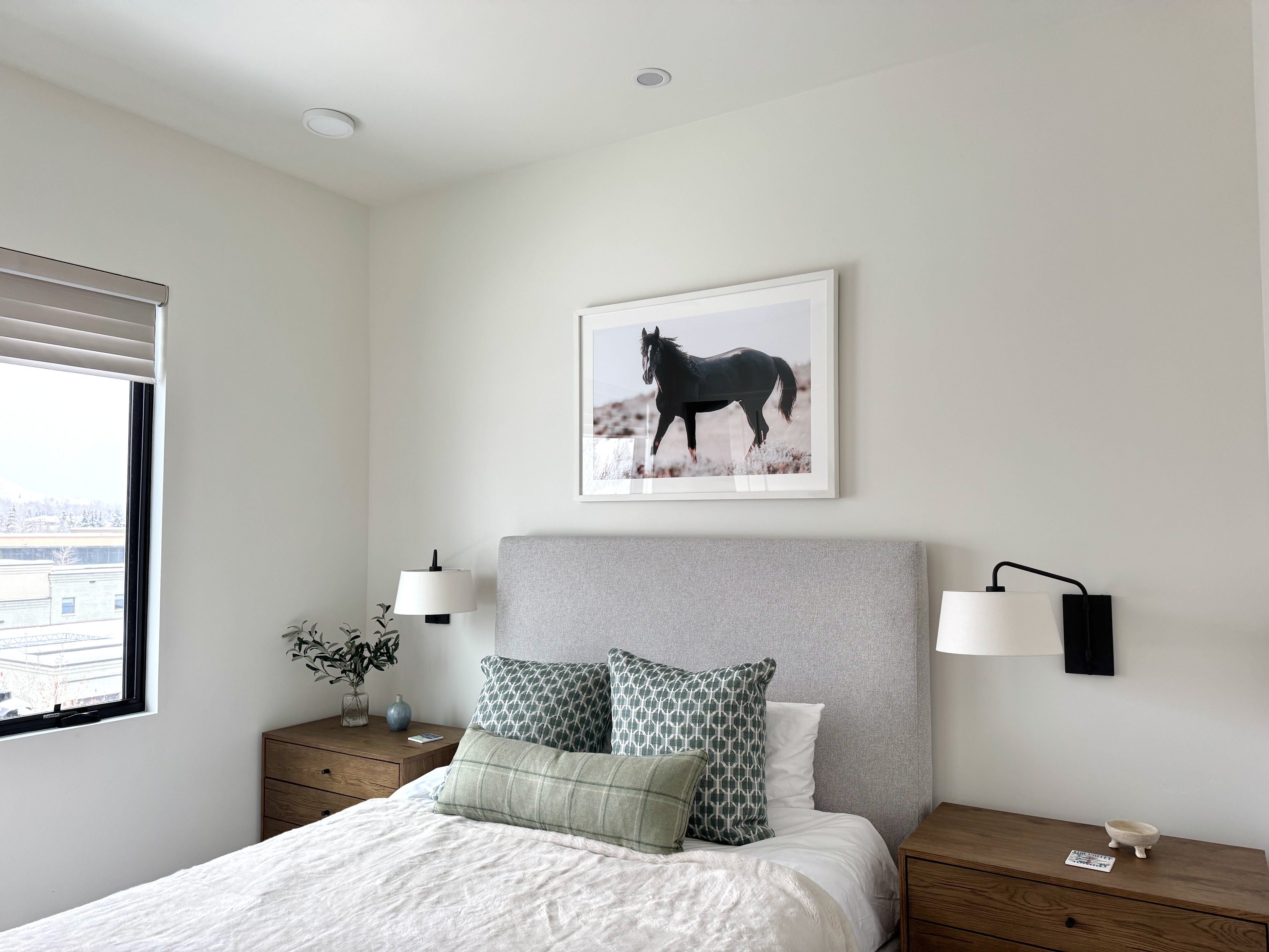 Modern bedroom with a bed, nightstands, and a horse painting on the wall.