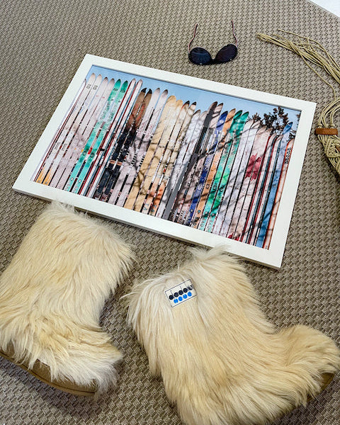 Pair of fluffy slippers with a framed artwork of feathers on a textured surface.