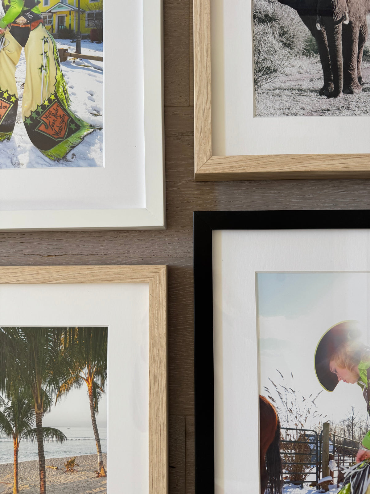 Framed wall art arranged on a wood-paneled wall, showing partial colorful photographs in light wood, black, and white frames.