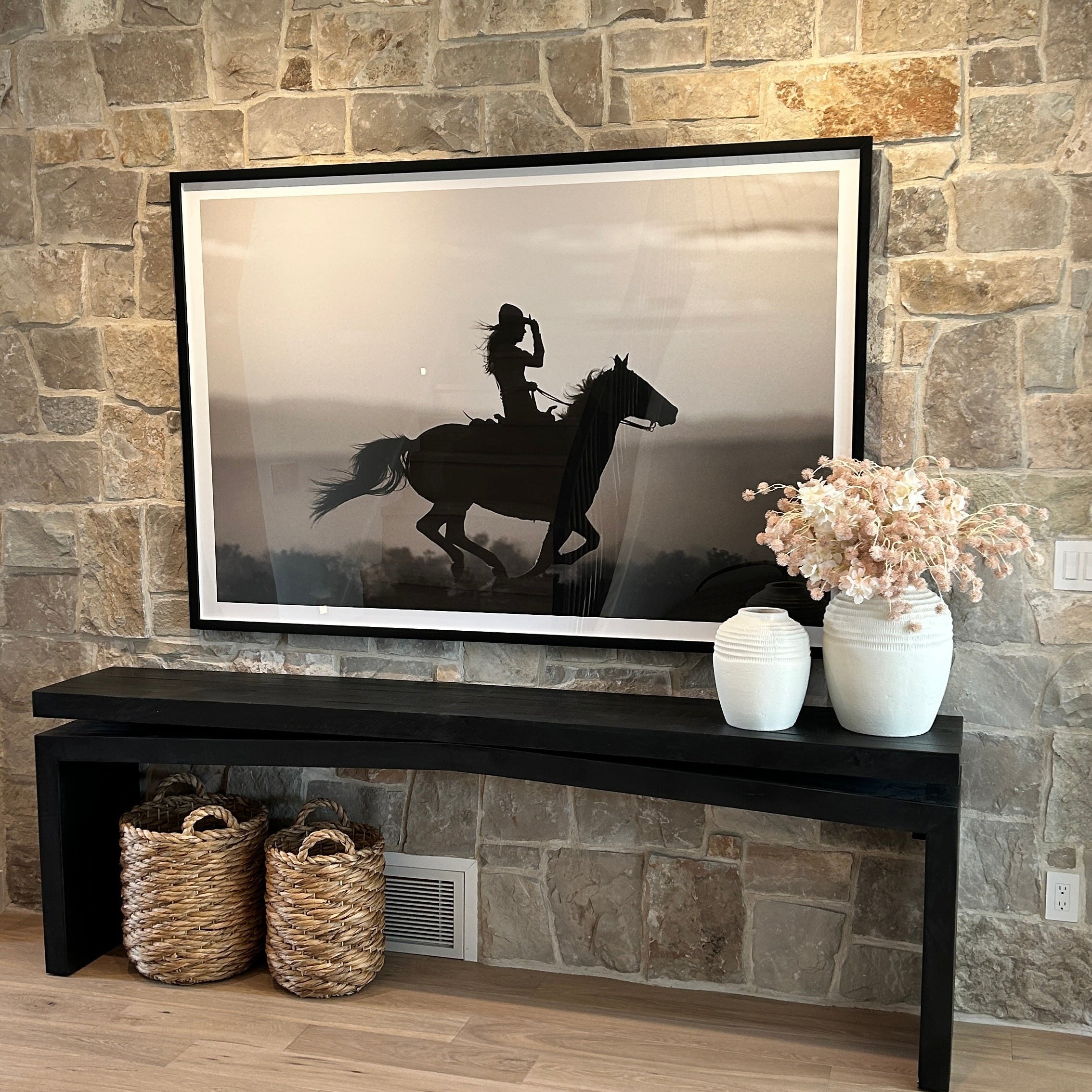 Framed artwork of a horse and rider on a stone wall with decorative items below.