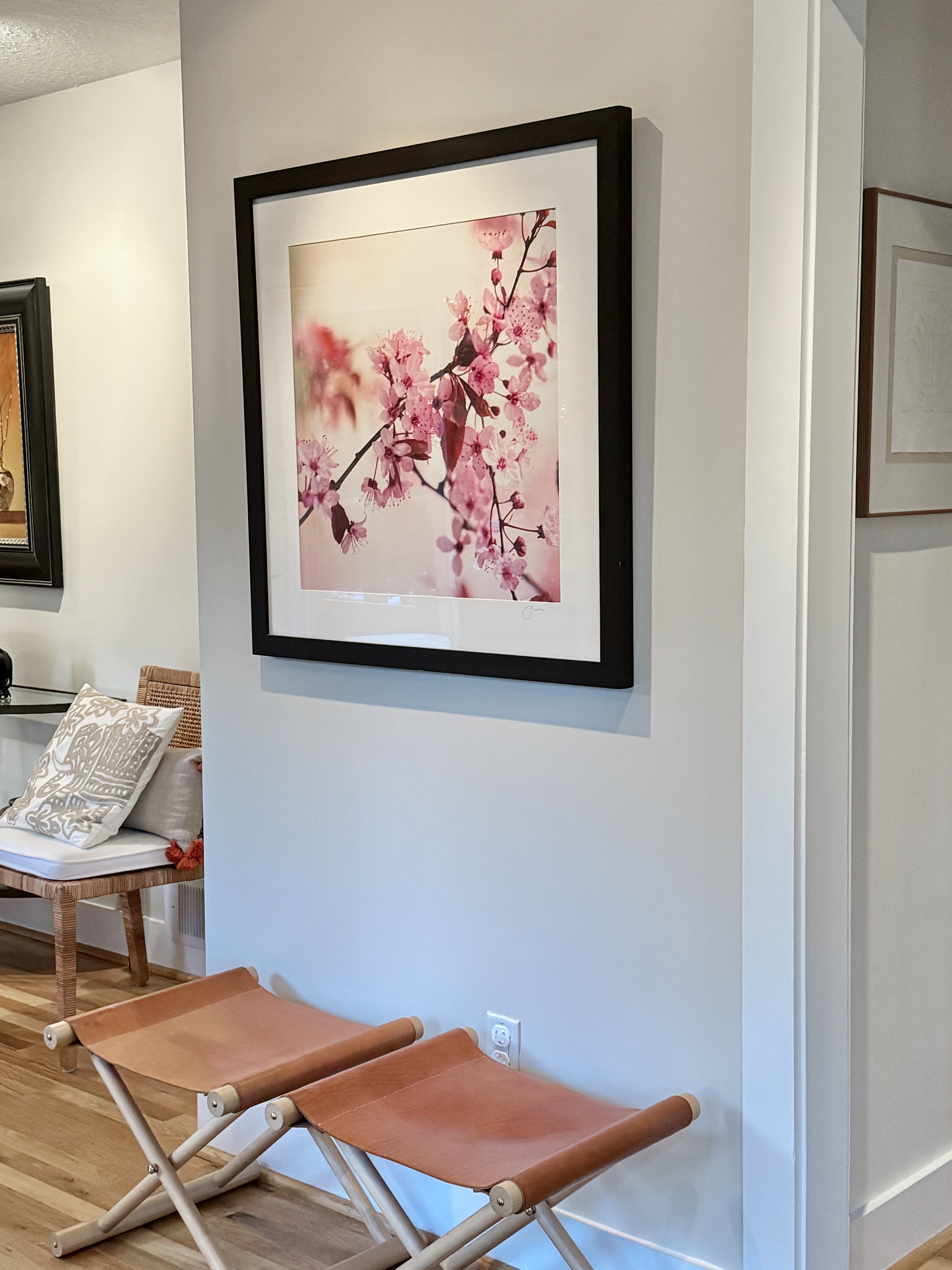 Framed artwork of cherry blossoms on a wall in a room with a stool and bench.