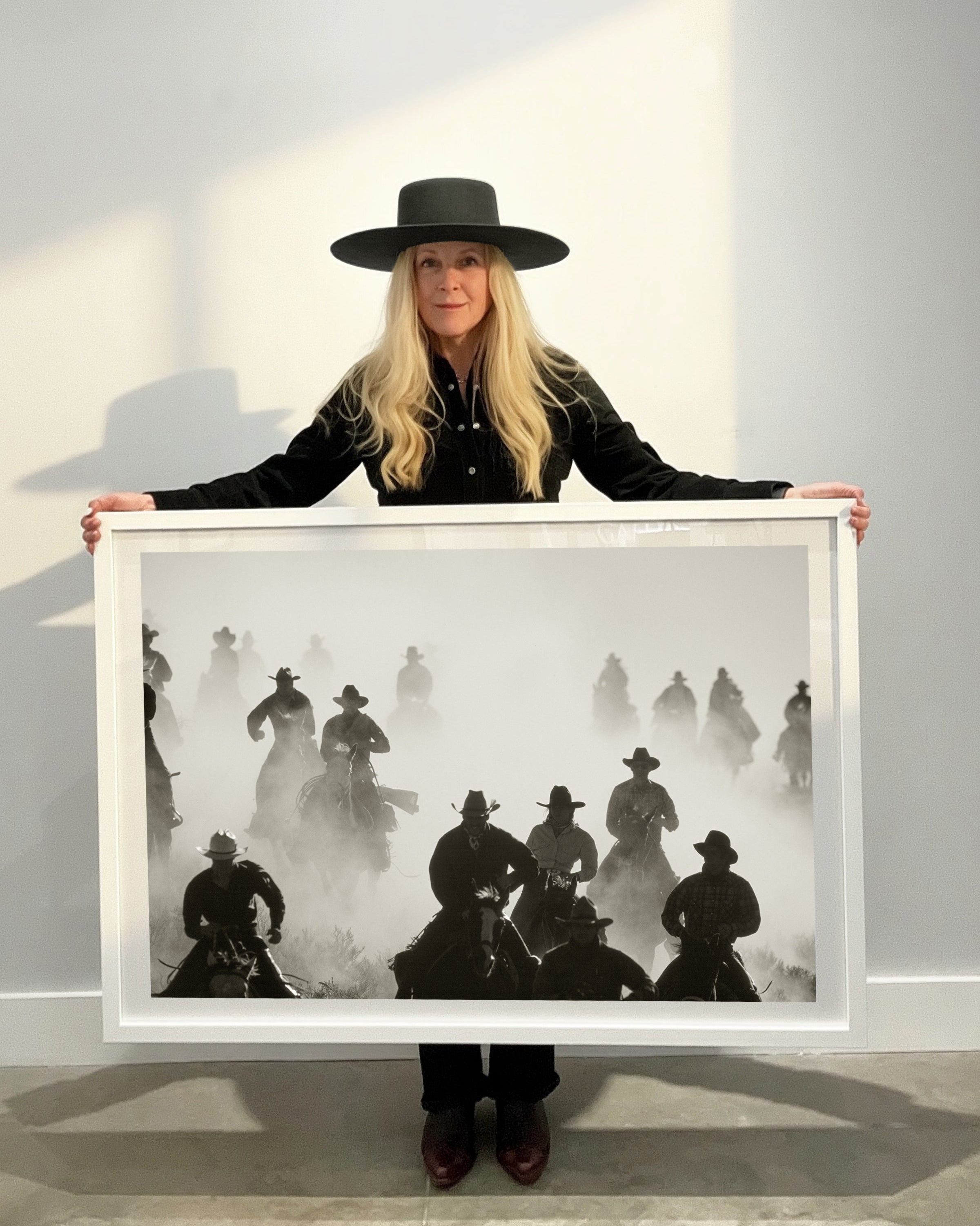 Person holding a framed black and white artwork of cowboys on horses.