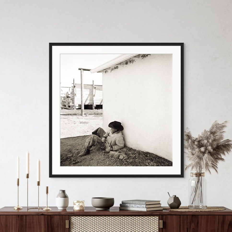 Cowboy Break, by Jules Frazier, Framed black and white photograph of a cowboy sitting at ranch. 